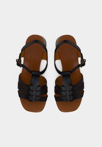 Μαύρα σανδάλια με λουριά και υφή, καφέ πέλμα, στρογγυλή πόρπη και ανοιχτή μύτη. Διακοσμημένα με γεωμετρικό σχέδιο στη σόλα.