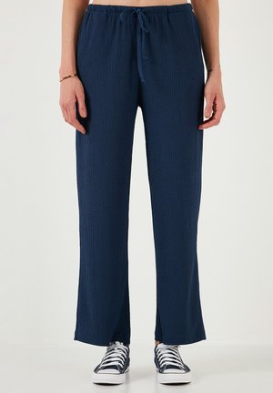Navy blue wide-leg pants with a ribbed texture, elastic waistband, and adjustable drawstring. Features slits at the ankle; paired with white sneakers.