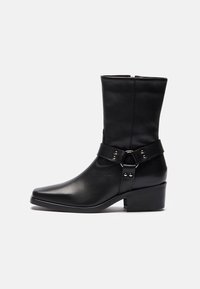 Zwarte leren enkellaars met een gestructureerd ontwerp, een vierkante neus, een zijrits en een decoratieve band met metalen hardware accenten.