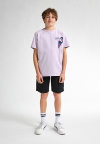 Lilla bomulds t-shirt med en blå og rød flamingo grafik på brystet, parret med sorte shorts, hvide sneakers og stribede ankelsokker.