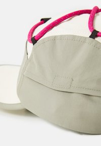 Cappello color khaki chiaro con una texture morbida, dotato di una corda intrecciata rosa brillante e accenti in hardware nero. Il design include una visiera curva.