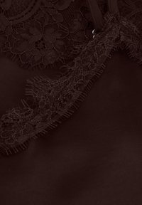 Vêtement marron foncé avec une bordure en dentelle complexe le long du bord, présentant une texture douce et des détails subtilement effilochés.