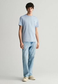 Světle modré bavlněné tričko s kulatým výstřihem, spárované se světle modrými džínami a béžovými teniskami. Jednoduchý a pohodlný střih.