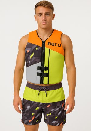 Homme portant un gilet de sauvetage coloré avec des motifs géométriques orange, vert citron et noir, assorti à un short de bain.