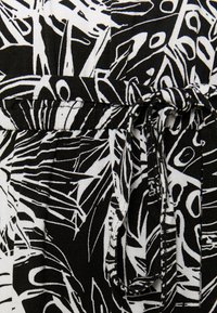 Zwart-wit gestippeld stof met abstracte lijnen en vormen, met een strikdetail in de taille voor aanpassing. Getextureerd, lichtgewicht materiaal.