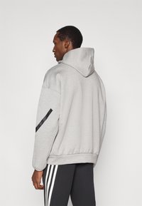 Pilkas gobtuvu megztinis laisvo silueto, ant rankovės juoda akcentinė juosta ir tekstūruota medžiaga. Priekyje kengūros tipo kišenė.