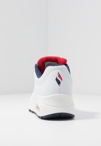 Bílé tenisky s texturovaným námořnickým a červeným límcem. Vyznačují se perforovanými detaily a akcentem loga na patě. Gumová podrážka s viditelnou vzduchovou jednotkou.