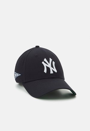 Black baseball cap made of cotton, featuring a white embroidered New York Yankees logo on the front and a side tag in blue and white.