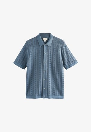 Camisa de manga corta con botones en azul claro. Presenta una textura con patrón de diamantes y un cuello sólido. Hecha de un material de punto suave.