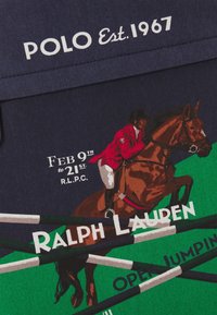 Marineblått tyg med en grafik av en häst och ryttare i röd jacka, med text i vitt och gr önt som anger evenemangsdatum och varumärke.