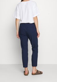 Pantalons slim-fit bleu marine avec poches arrière, assortis à un haut blanc ample à manches courtes et des sandales marron.