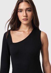 Musta, yhdellä olkapäällä varustettu toppi, valmistettu sileästä kankaasta. Siinä on istuva muotoilu ja syvä, vino sauma rinnan yli kulkevalla leikkauksella.