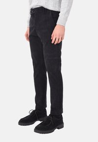 Pantaloni in corduroy neri con una vestibilità slim, dotati di chiusura con bottone e una sottile texture a coste, abbinati a scarpe in suede nere.