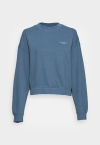 Sudadera azul corta hecha de material suave, con cuello redondo, mangas largas y un pequeño logo blanco en el frente.