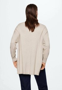 Pull oversize beige clair avec manches longues, poignets côtelés et coupe décontractée, vu de dos sur un fond uni.