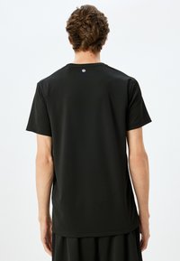 Czarny t-shirt sportowy z krótkim rękawem, gładką fakturą, okrągłym dekoltem oraz małym logo na górnej części pleców.