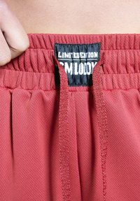 Red athletic shorts with an elastic waistband, featuring a visible drawstring and a black label that reads "LIMITED EDITION" in white.