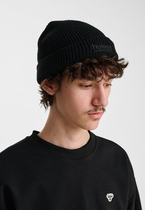 Sort ribbet strikket beanie med opfoldet kant og tekstureret materiale; båret sammen med en sort crewneck sweatshirt med et lille logo.