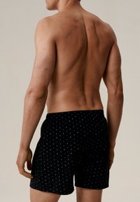 Czarne bokserki w małe niebieskie i białe kropki, wykonane z miękkiego materiału. Elastyczny pas, luźny krój, widoczne detale przeszycia.