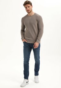 Lichtbeige gebreide trui met een ronde hals, gecombineerd met blauwe denim jeans en witte sneakers met zwarte accenten.