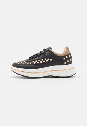 Sort sneaker med guldnitter, tyk hvid sål med gylden stribe og tan stofhælkant med subtilt mønster.