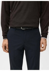 Ciemnobrązowy sweter z długim rękawem w połączeniu z granatowymi spodniami, z srebrną metalową klamrą paska i gładką fakturą tkaniny.