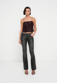 Crop top bordeaux à sequins avec fines bretelles, associé à un jean noir évasé avec ceinture cloutée, et des talons noirs à lanières.