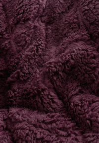 Dybt lilla tekstureret stof med tætte, bløde, krøllede fibre, der skaber et blødt, hyggeligt udseende og ujævne overflademønstre.