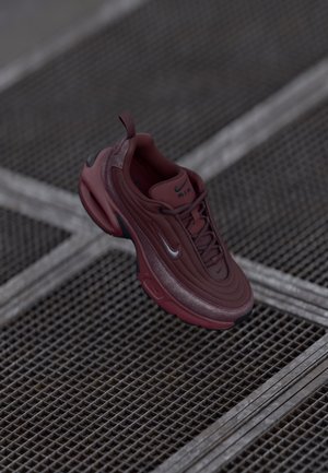 Bordo spalvos sportbačiai su tekstūruota paviršiumi ir išlenktu dizainu. Apima sidabrinį logotipą, raištelius ir paminkštintą padas. Lengva konstrukcija.