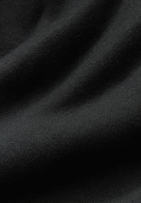 Sort stof med en glat tekstur, der har et subtilt ribbet mønster og bløde draperinger, hvilket indikerer et let strikkemateriale.