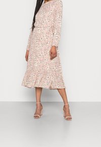 Květinové midi šaty v jemně růžové barvě s dlouhými rukávy, volným střihem a nabíraným lemem. Obsahují jemný květinový vzor a hladkou texturu látky.