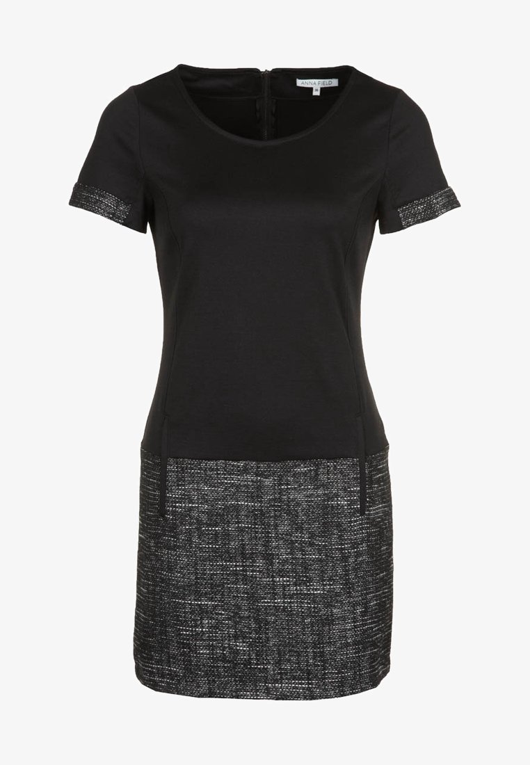 Robe noire à manches courtes, avec un ourlet texturé en noir et blanc. Confectionnée dans un tissu lisse, elle possède un col rond et une fermeture éclair.