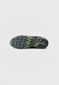 Semelle d'une basket Puma noire et verte avec une accroche texturée et un logo visible au niveau du talon.