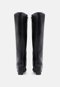 Bottes en cuir noir montantes avec une texture lisse et des talons carrés, dotées de fermetures éclair sur les côtés et d'un design épuré.