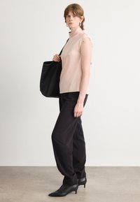 Top senza maniche rosa chiaro abbinato a pantaloni neri, forma strutturata, texture liscia, décolleté neri a punta e borsa tote nera.