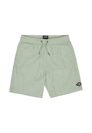 Blond chłopiec stojący, ubrany w jasnoniebieską, wzorzystą koszulę na guziki z krótkim rękawem, miętowe krótkie spodenki, czarne skarpetki oraz czarne trampki.