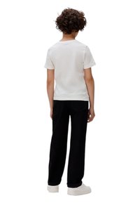 Camiseta blanca de manga corta y pantalones anchos negros, usados con zapatillas de plataforma blancas. Pelo rizado visible desde atrás.