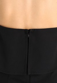 Czarna dopasowana bluzka z gładkiego materiału, z tylnym zapięciem na zamek i dołem w stylu peplum. Czyste linie i minimalistyczne detale.