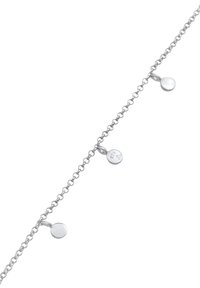 Bracelet en chaîne en argent avec trois petits pendentifs ronds, dont un estampillé d'un logo, texture lisse et design délicat.