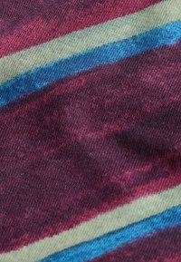 Gros plan sur un tissu à rayures horizontales rouge bordeaux, beige et bleu, montrant une texture de tricot détaillée et des transitions de couleur.