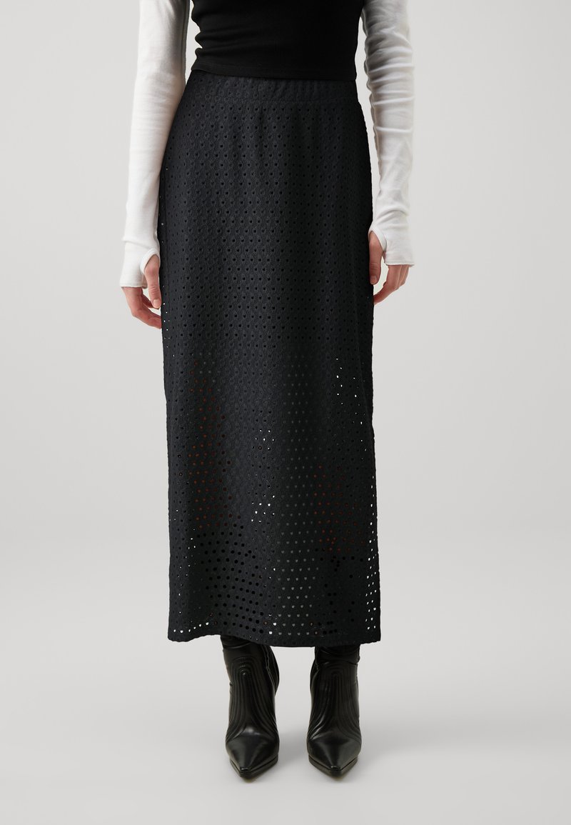 Black perforated maxi skirt featuring a textured pattern. High waistband, straight shape, paired with black ankle boots.