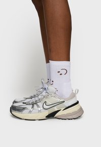 Buty sportowe z połączeniem srebrnej siateczki i beżowej skóry. Gruba czarna podeszwa; szare sznurówki. Białe skarpety z brązowymi akcentami.