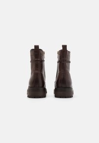 Une paire de bottines en cuir marron foncé avec des talons carrés, vue arrière sur un fond blanc uni.