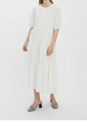 Robe blanche jusqu'aux genoux avec manches bouffantes, encolure ronde et fermeture à boutons. Texture ajourée sur toute la surface et ourlet à volants. Accessoirisée avec des chaussures vertes.