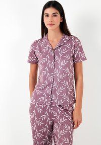 Pijama set kratkih rukava u umirujuće mauve boji s bijelim uzorcima lišća. Sadrži košulju s ovratnikom i gumbima sprijeda te odgovarajuće hlače, izrađene od lagane tkanine.