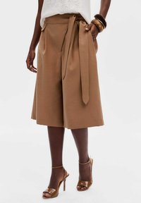 Bruine brede broek met een strik taille, gladde stof en zijzakken, gecombineerd met bruine open teen hakken.