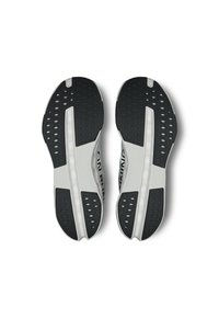 Des chaussures de course avec une semelle principalement noire et blanche, présentant des motifs en caoutchouc texturé et des trous de drainage pour une adhérence et une flexibilité optimales.