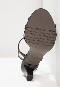 Sandale noire à talons hauts avec brides à la cheville, semelle portant le logo "Tamaris" en répétition, taille 37, vue du dessous sur fond blanc.