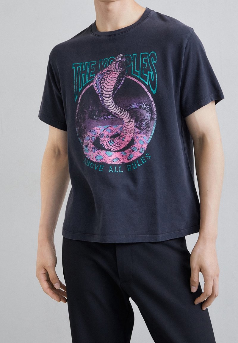 Černé bavlněné tričko s grafikou hadu, který se vine, v růžové a tyrkysové barvě, s textem "THE KOOPLES" a "ABOVE ALL RULES." Krátké rukávy.