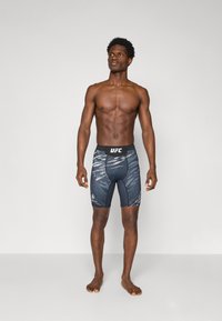 Shorts compressivi UFC neri e grigi con una vestibilità aderente, caratterizzati da un motivo a onde distintivo e un logo sulla vita.